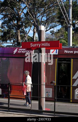 A woman on the platform as a passenger alights the tram at the Light Rail stop on Devonshire Street, Sydney with the Surry Hills sign Stock Photo