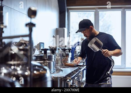 Standing in brewery, technologist taking notes during checking brewing process and equipment. Science and craft in beer production. Stock Photo