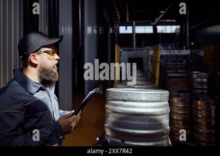 Kegging Process Concentrated man, brewery technologist, equipped with safety glasses ...