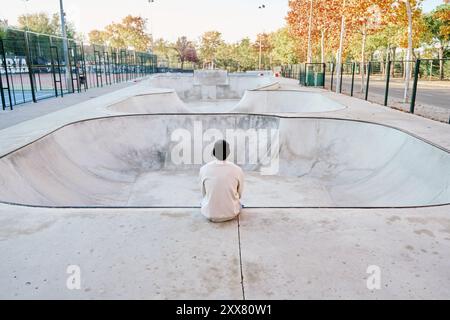 unrecognizable man sitting on a ramp thinking while looking at a vacant skatepark Stock Photo