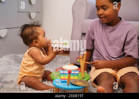 Older brother playing music with baby sister using colorful toy Stock Photo