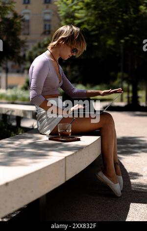 Woman using laptop while sitting on bench. Stock Photo