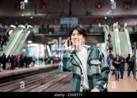 young attractive asian man talking to friends on the phone before going on a journey through Europe by train. man is calling on the phone before headi Stock Photo