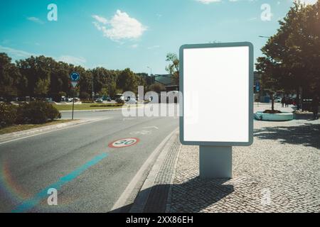 Outdoor billboard mockup on a roundabout, with a clear blue sky and surrounding greenery in a suburban area. The blank white advertising space is read Stock Photo