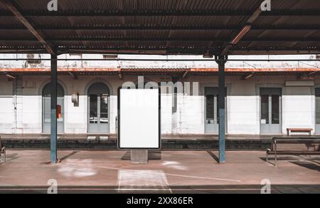 Empty suburban train station platform with a blank billboard mockup in the center. The scene features a rustic, partially covered area with metal colu Stock Photo