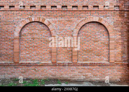 The brick wall features two distinct arched openings, showcasing a textured red surface against a grassy backdrop. Stock Photo