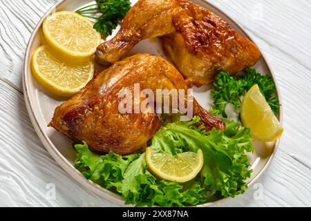 fried chicken legs served with lettuce, parsley, lemon wedges on plate on white wooden table, close-up Stock Photo