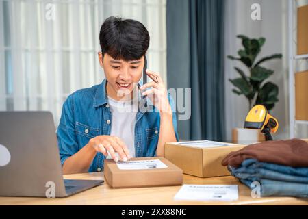 Happy young online seller man talking to his customer on the phone while checking the shipping label information on the product box Stock Photo