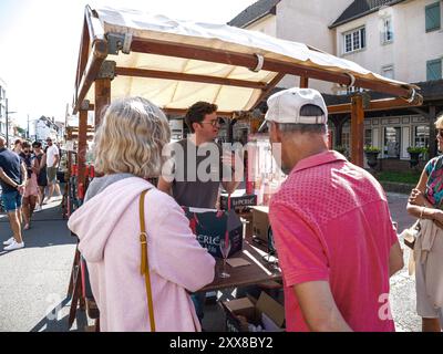 Hardelot, France - Aug 20, 2023: A vendor engages in conversation with customers at a market stall in Neufchatel-Hardelot, France, while displaying bottles of wine and beer Stock Photo