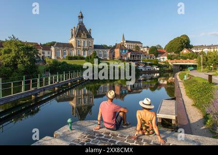 France, Somme, Valley of the Somme, Long, the banks of the Somme along the river, couple looking towards the town hall and the Saint Jean-Baptiste church Stock Photo