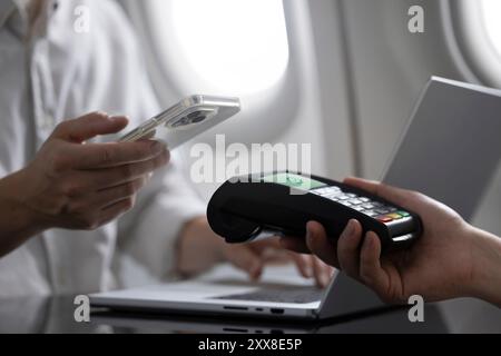 A man is making a purchase on an airplane using convenient mobile payment with contactless tap-to-pay technology. The image captures the ease and effi Stock Photo