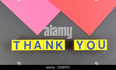 Thank you word above wooden cubes style and black background with red and pink colors triangle shape. Stock Photo