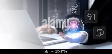 The businessman sits at a desk in a data center, working on his laptop. He extends his palm, and a transparent sphere appears, within which a hologram Stock Photo