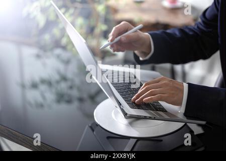 A businessman is focused on his laptop at an office desk, immersed in his tasks. The office setting is professional, with documents and essential work Stock Photo
