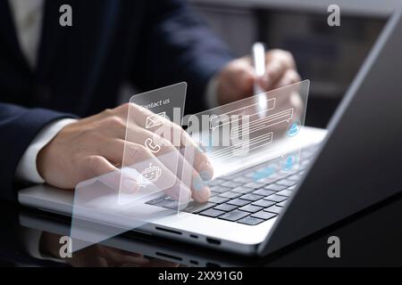 A businessman works on his laptop, interacting with an online customer service chatbot displayed as a hologram. The chatbot assists with prompt and ef Stock Photo