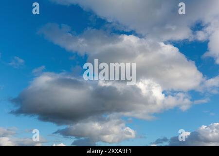 Dark, fluffy clouds that dance against a vibrant blue backdrop, casting intriguing shadows below Stock Photo