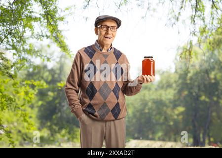 Elderly man holding a jar of honey and smiling outdoors Stock Photo