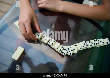 A close-up of a person's hands skillfully arranging dominoes on a glass table, embodying strategic thinking and casual entertainment. Stock Photo
