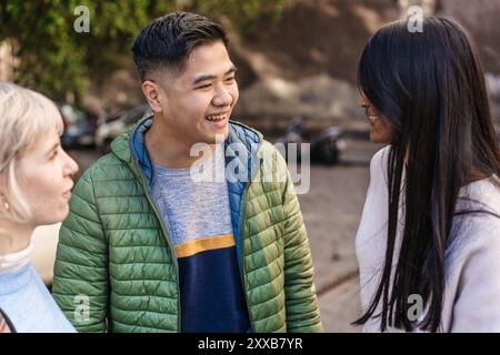Candid portrait of a cheerful young Asian man laughing with his diverse group of friends in an outdoor setting. Young adults authentic representation Stock Photo