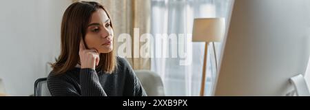 A young woman in a grey sweater sits thoughtfully in a home office, contemplating her next creative project. Stock Photo