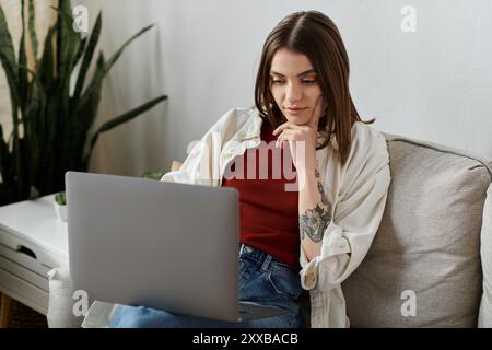 A young woman in casual attire sits on a couch, using a laptop to manage her social media accounts. Stock Photo