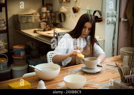 Young female ceramist in the workshop making mug out of clay Stock Photo