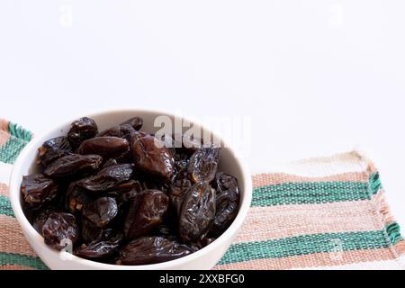 White ceramic bowl filled with dried dates on top of a striped placemat. Stock Photo