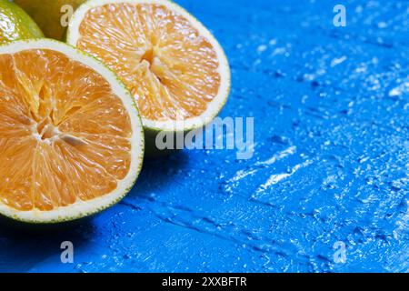 Two orange halves with the pulp reflecting the light and lying on a blue table. Stock Photo