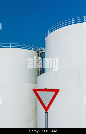 Give way traffic sign in front of white oil tank plants Stock Photo