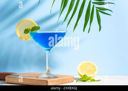 Blue summer cocktail with mint and lemon on sky blue background with palm leaf. Trendy creative concept. Cocktail blue lagoon with curacao liqueur. Stock Photo
