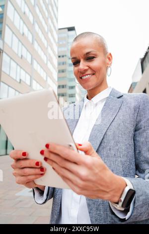 Vertical self-assured businesswoman is using a tablet at a downtown workplace. Executive browsing the internet with a touchpad and a communication app, embodying the successful entrepreneur spirit. High quality photo Stock Photo