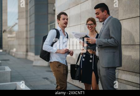Professional meeting of three young professionals standing outdoors discussing work in a bustling urban setting, engaging in a collaborative business Stock Photo