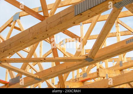 Wooden roof trusses and beams form a complex structure against a blue sky, illustrating the intricacies of modern construction techniques and craftsma Stock Photo