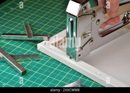 Heavy duty industrial stapler. Canvas installation on wood frame. Construction stapler for DIY home improvement. Staples strips and stapler gun for re Stock Photo
