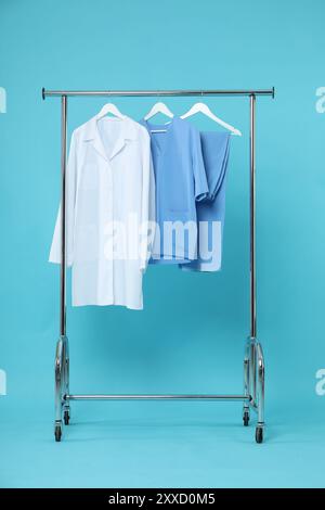 Different medical workers' uniforms on clothing rack against light blue background Stock Photo