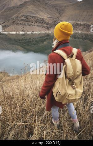 A portrait from the back of a girl traveler on the background of a lake in the mountains in autumn or early spring. Travel concept Stock Photo