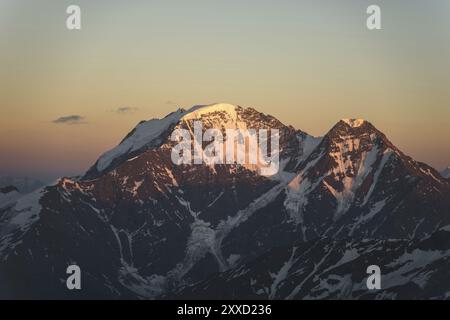 A sunset panorama of the elbrus and part of the Caucasian ridge with orange clouds and a cracked glacier at the bottom Stock Photo