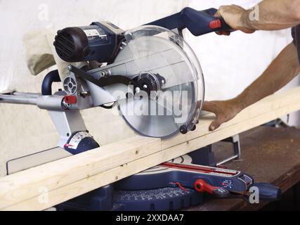 Closeup of hands of a person cutting wood lumber with a mitre saw, miter saw, circular blade Stock Photo