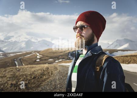Hipster young man with beard and mustache wearing sunglasses posing against the background of mountains Stock Photo