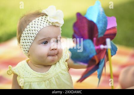 Baby playing with windmill toy in backyard on a blanket. Summer day outdoors. Background Stock Photo