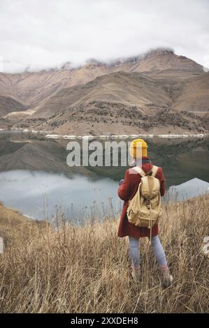 A portrait from the back of a girl photographer traveler on the background of a lake in the mountains in autumn or early spring. Travel concept Stock Photo