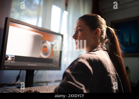 A young woman is sitting at a computer in the office, doing graphic design Stock Photo