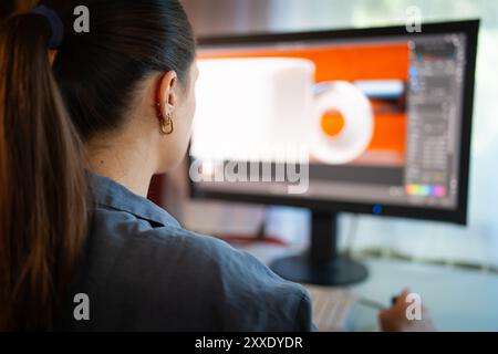 A young woman is sitting at a computer in the office, doing graphic design Stock Photo