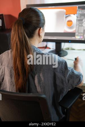 A young woman is sitting at a computer in the office, doing graphic design Stock Photo