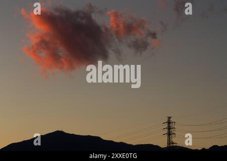 A colourful clouds catches sunset light above mountains and an electricity pylon in Kanagawa, Japan. Stock Photo
