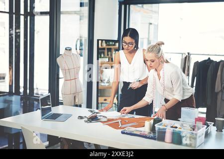Women, fashion and designers with garment at workshop for material, design or teamwork at office. Young, female person or tailors working together on Stock Photo