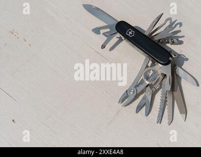 A Swiss Army knife Victorinox Swiss Champ with many different tools on it. The knife is black and silver. The knife is laying on a white surface Stock Photo