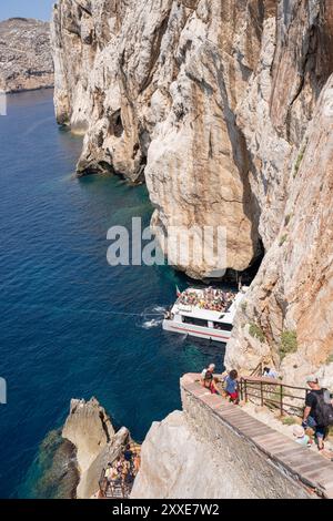 Alghero, Italy - August 25, 2023: Tourists accessing the Grotto of Neptune (Grotta di Nettuno) on foot via the steep stairs and by boat directly into Stock Photo