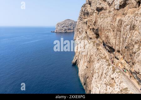 Seascape with the great cliff with people walking in the corridor to access to the Neptune's Grotto (Grotta di Nettuno) dug in the in the middle of th Stock Photo