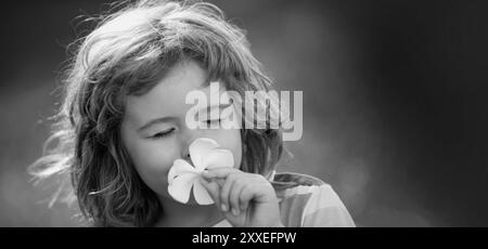 Close up face of cute child outdoors. Spring banner for website header. Funny child smelling plumeria flower, face close up. Kids in summer nature Stock Photo